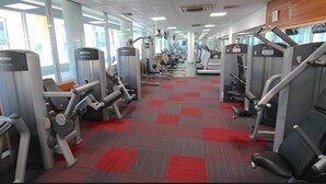 Une salle de sport équipée de divers appareils d’exercice, dotée d’un sol recouvert d’une moquette rouge et de grandes fenêtres laissant entrer la lumière naturelle.