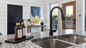 A modern kitchen with a granite countertop, a black faucet, and two hand soap bottles on a soap dish. - Cozy River Getaway W/ Heated Pool, Pool Table, Kayaks, Fishing | EV (Broken Bow)