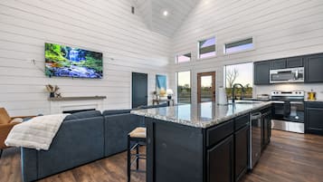 A modern kitchen with a large island, dark cabinetry, and a flat-screen TV mounted on the wall.