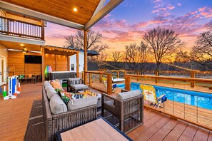 A covered outdoor deck with a pool, seating area, and a view of the sunset.