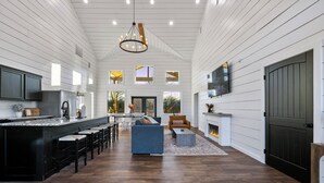 A spacious kitchen with a central island, a dining area with a large window, and a cozy seating area with a fireplace. - Cozy River Getaway W/ Heated Pool, Pool Table, Kayaks, Fishing | EV (Broken Bow)