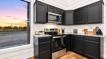 Modern kitchen with dark cabinets, stainless steel stove and microwave, and countertop cooking tools—ready for easy breakfasts or homemade group dinners.