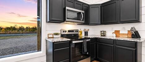 A modern kitchen with black cabinets, stainless steel appliances, and a large window offering a view of the outdoors.