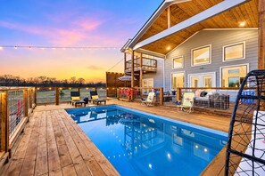 Terraza de madera con piscina, mobiliario exterior y un área cubierta con vistas al paisaje.