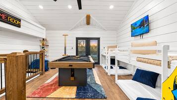 Une table de billard dans une pièce équipée de lits superposés et d’un téléviseur fixé au mur.