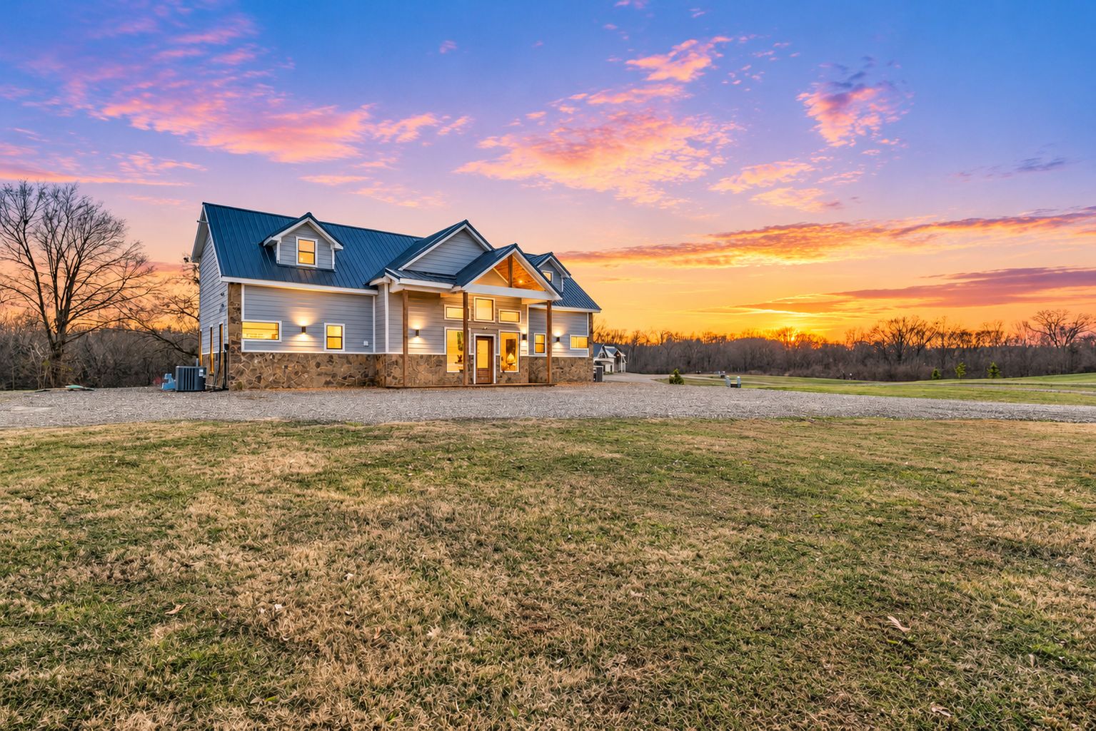 Our driveway fits up to 5 cars and a boat. Golden-hour view of the farmhouse-style exterior, with a covered entry, warmly lit windows, and an open yard at this peaceful Broken Bow vacation cabin.