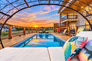 Unwind beside the private swimming pool with deck seating, warm evening lighting, and colorful sunset skies. Pool heating is available by request for an added fee.