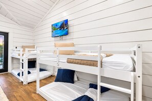 A bunk room with white wooden walls, a television mounted above the beds, and a view through the door. - Cozy River Getaway W/ Heated Pool, Pool Table, Kayaks, Fishing | EV (Broken Bow)