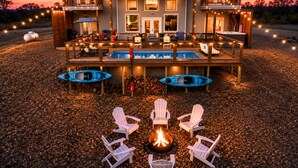 A two-story house with a deck, outdoor seating, kayaks, and a fire pit. - Cozy River Getaway W/ Heated Pool, Pool Table, Kayaks, Fishing | EV (Broken Bow)