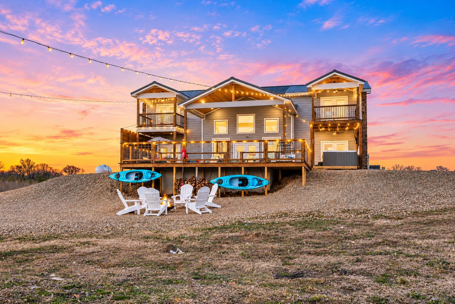 A two-story house with a deck, outdoor seating, kayaks, and a scenic sunset view.