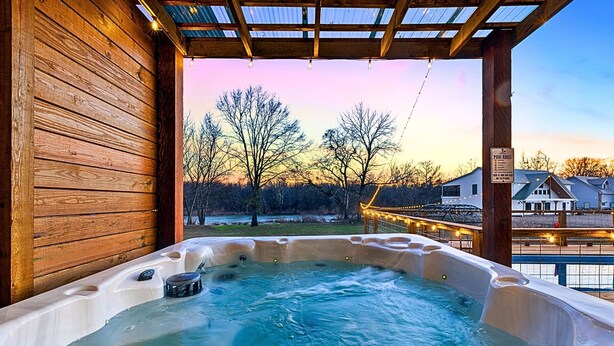 A hot tub with a wooden exterior and a view of trees and houses in the background. - Cozy River Getaway W/ Heated Pool, Pool Table, Kayaks, Fishing | EV (Broken Bow)