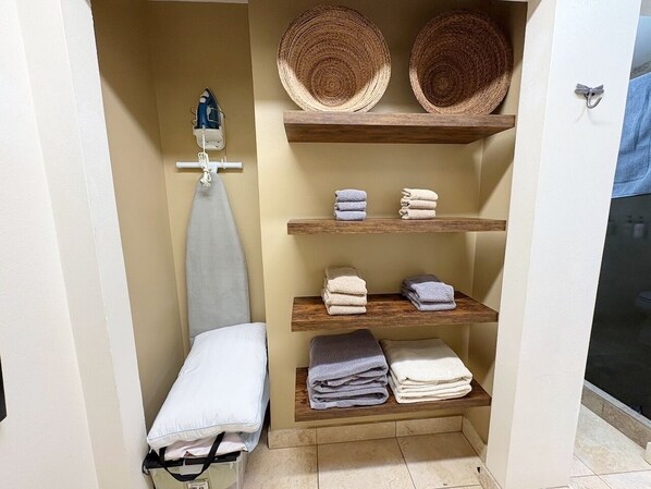 A bathroom with a towel rack, shelves with folded towels, and a hanging hat.