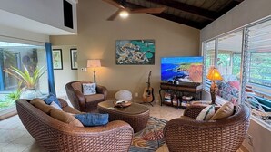 A living room with wicker furniture, a television, and a ceiling fan. - Hale Haku Home- Unbelievable Ocean Views! (Kailua-Kona)