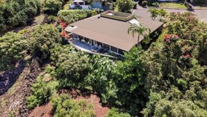A modern house with a flat roof, surrounded by dense greenery and a paved driveway. - Hale Haku Home- Unbelievable Ocean Views! (Kailua-Kona)