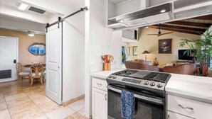 A modern kitchen with a stove, cabinets, and a sliding door leading to a dining area. - Hale Haku Home- Unbelievable Ocean Views! (Kailua-Kona)