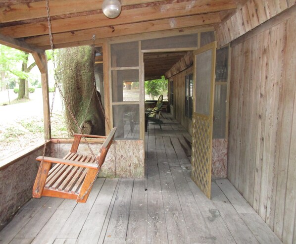 A wooden porch with a swing, a view of the outdoors, and a covered seating area.