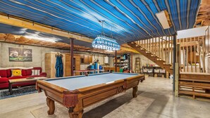 Une pièce spacieuse avec une table de billard, un canapé rouge et un escalier en bois.