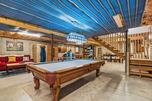 A spacious room with a pool table, a red sofa, and a wooden staircase.