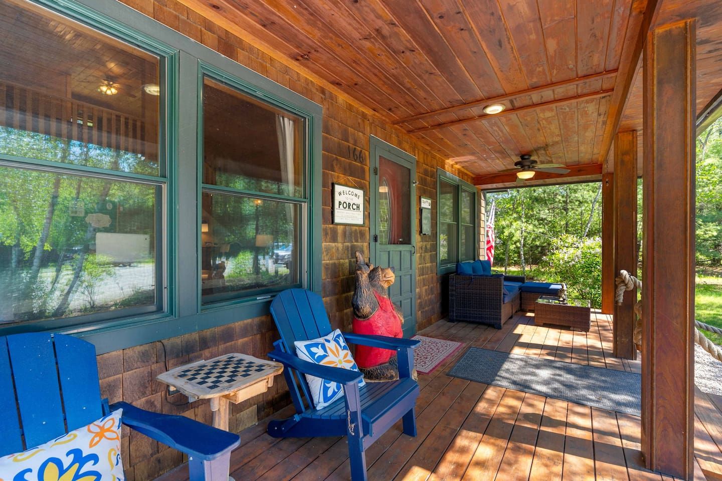 A wooden porch with blue chairs, a checkered table, and a welcome sign.