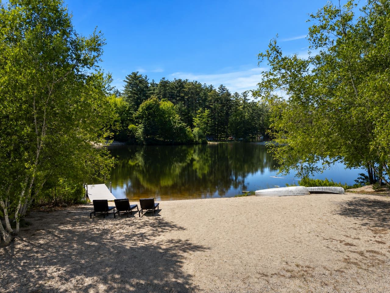 A lakeside campsite with a sandy area, two chairs, and a covered picnic table.