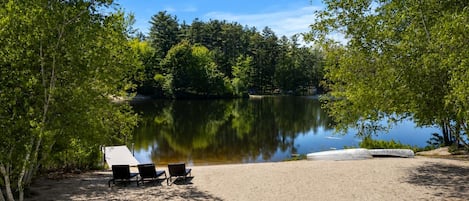 A lakeside campsite with a sandy area, two chairs, and a covered picnic table.