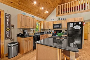 A kitchen with wooden cabinets, a black refrigerator, and a welcome sign.