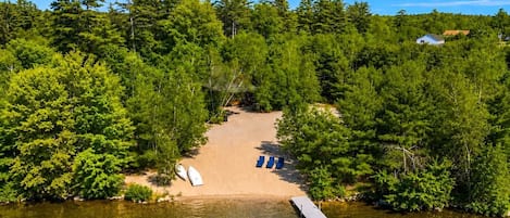 A lakeside property with a sandy beach, a dock, and a row of blue lounge chairs.