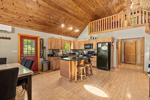 Una cocina amplia con armarios de madera, una isla central con taburetes, un refrigerador negro y una puerta roja.