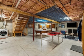 Un sótano con mesa de ping pong, lavadora, escalera y mesa de billar.