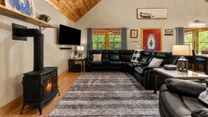 Un salon chaleureux avec une cheminée, un canapé en cuir noir, un téléviseur et un coin repas comprenant une table et des chaises.
