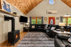 A cozy living room with a fireplace, a black leather sofa, a television, and a dining area with a table and chairs.