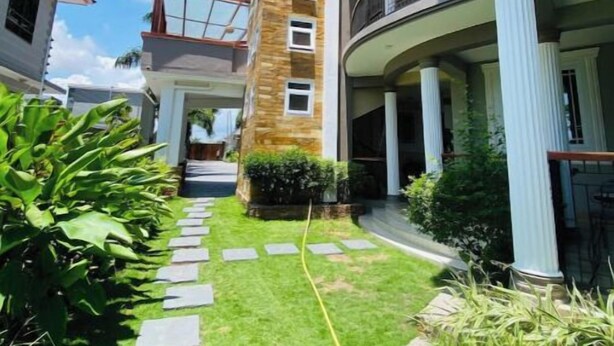 A modern building with a central courtyard, stone steps leading to a door, and a well-maintained lawn. - New and stylish 3-Bedroom Apartment (Dar es Salaam)