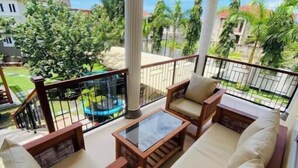 A balcony with wicker furniture, a glass-top table, and a view of a residential area with palm trees and houses. - New and stylish 3-Bedroom Apartment (Dar es Salaam)