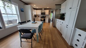 A modern kitchen with white cabinets, a dining table with chairs, and a view of the ocean through large windows. - 3 BR Lake Front Getaway! Dog Friendly, Lakeside Deck, Dock, Incredible Sunrises (Alpena)