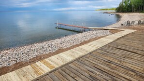 A wooden pier extending into calm waters, surrounded by a pebbly shore and a forested area. - 3 BR Lake Front Getaway! Dog Friendly, Lakeside Deck, Dock, Incredible Sunrises (Alpena)