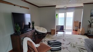 A living room with a flat-screen TV, a brown leather chair, a white armchair, a patterned rug, and a view of the ocean through a large window. - 3 BR Lake Front Getaway! Dog Friendly, Lakeside Deck, Dock, Incredible Sunrises (Alpena)