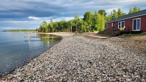 A lakeside property with a dock, a wooden deck, and a red building with large windows. - 3 BR Lake Front Getaway! Dog Friendly, Lakeside Deck, Dock, Incredible Sunrises (Alpena)