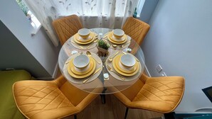 A dining table set for four with yellow chairs, a glass table, and a white curtain with leaf patterns.