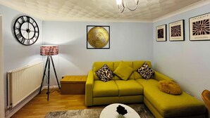 A living room with a green sofa, a round clock, and abstract art on the walls.