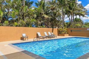 A swimming pool with lounge chairs and palm trees.