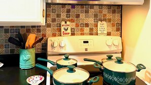 Une cuisine avec des meubles blancs, un four à micro-ondes, une cuisinière avec des casseroles et une pancarte sur laquelle on peut lire : « Bienvenue à la Coop ».
