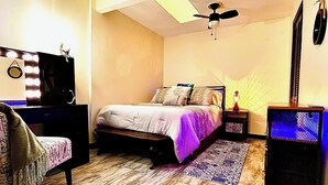 Une chambre à coucher comprenant un lit, une table de chevet, une commode, un ventilateur de plafond et un téléviseur fixé au mur.