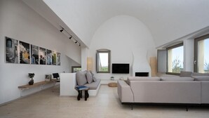 Amplia sala de estar con un sofá grande, una mesa de centro y un televisor de pantalla plana. Varias ventanas ofrecen luz natural y vistas al exterior.
