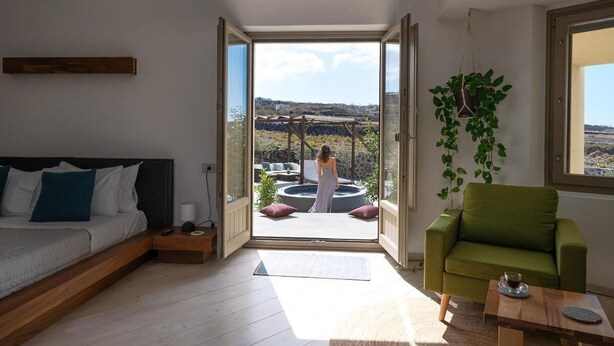 Un dormitorio moderno con cama, un sillón verde y vistas a un área con bañera de hidromasaje al aire libre.