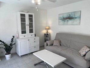 A living room with a white cabinet, a grey sofa, a white coffee table, a lamp, and a painting on the wall. - Garden studio 150 m from the beach (Fréjus)