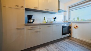 A modern kitchen with white cabinets, a built-in oven, and a window with a view of trees. - Central feel-good apartment 1 - ideal for your vacation or business trip (Magdeburg)