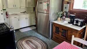 A compact kitchen with white cabinets, a stainless steel refrigerator, a coffee maker, and a toaster on the counter. - Charming 5-bedroom Roaring Brook cottage in Harbor Springs with beach access. (Harbor Springs)