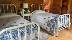 Two single beds with white metal frames and blue patterned bedding, a bedside table with a lamp and vase, and a wooden staircase in the background. - Charming 5-bedroom Roaring Brook cottage in Harbor Springs with beach access. (Harbor Springs)