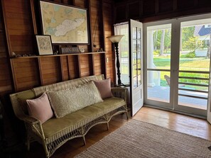 Een gezellige kamer met een rieten bank, een kaart aan de muur en uitzicht op een tuin door een glazen deur.