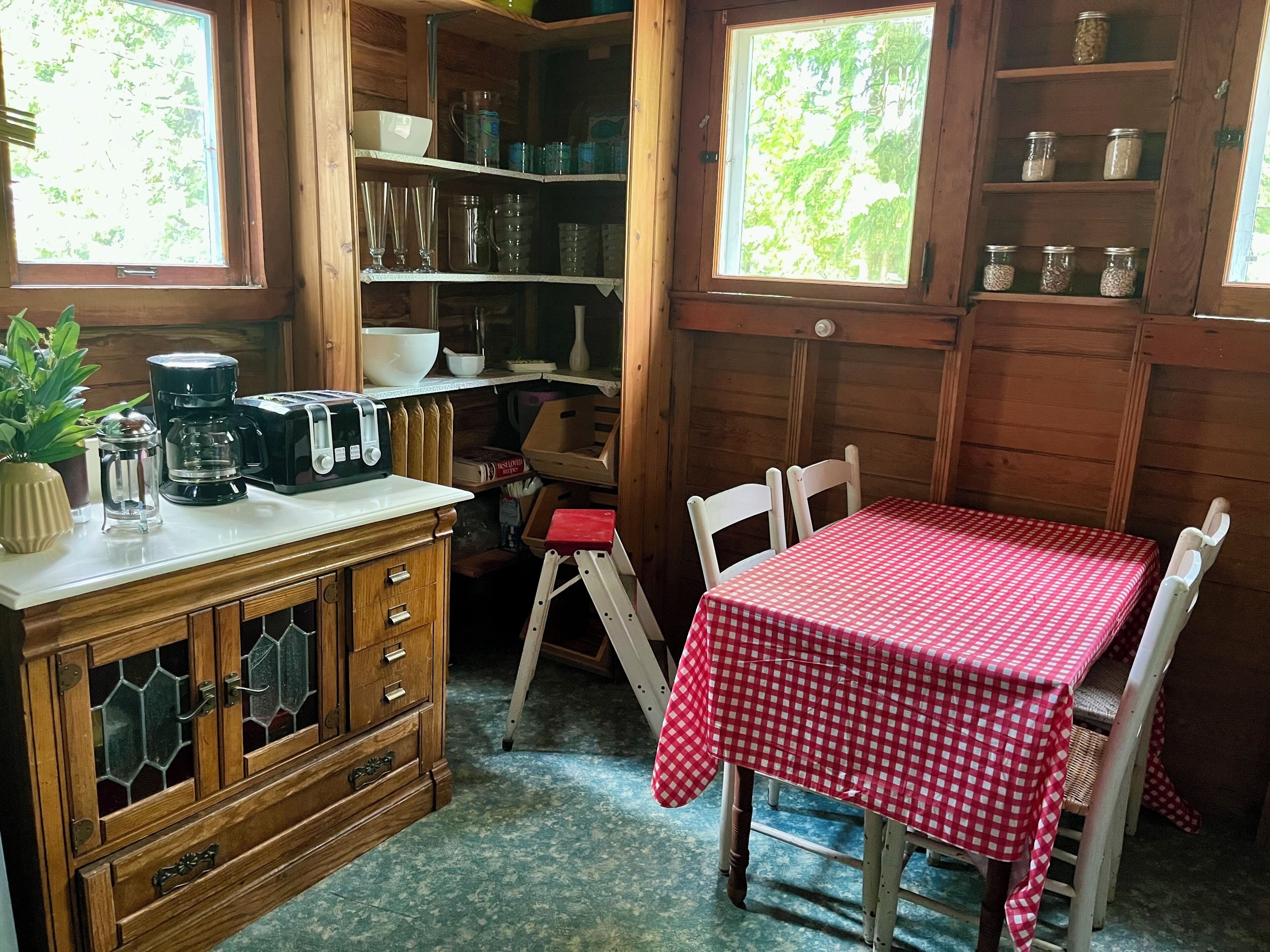Une cuisine compacte avec des meubles en bois, une machine à café et une table recouverte d’une nappe à carreaux rouges.